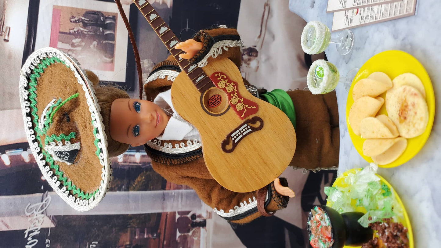 Doll with guitar and sombrero in front of a table with food