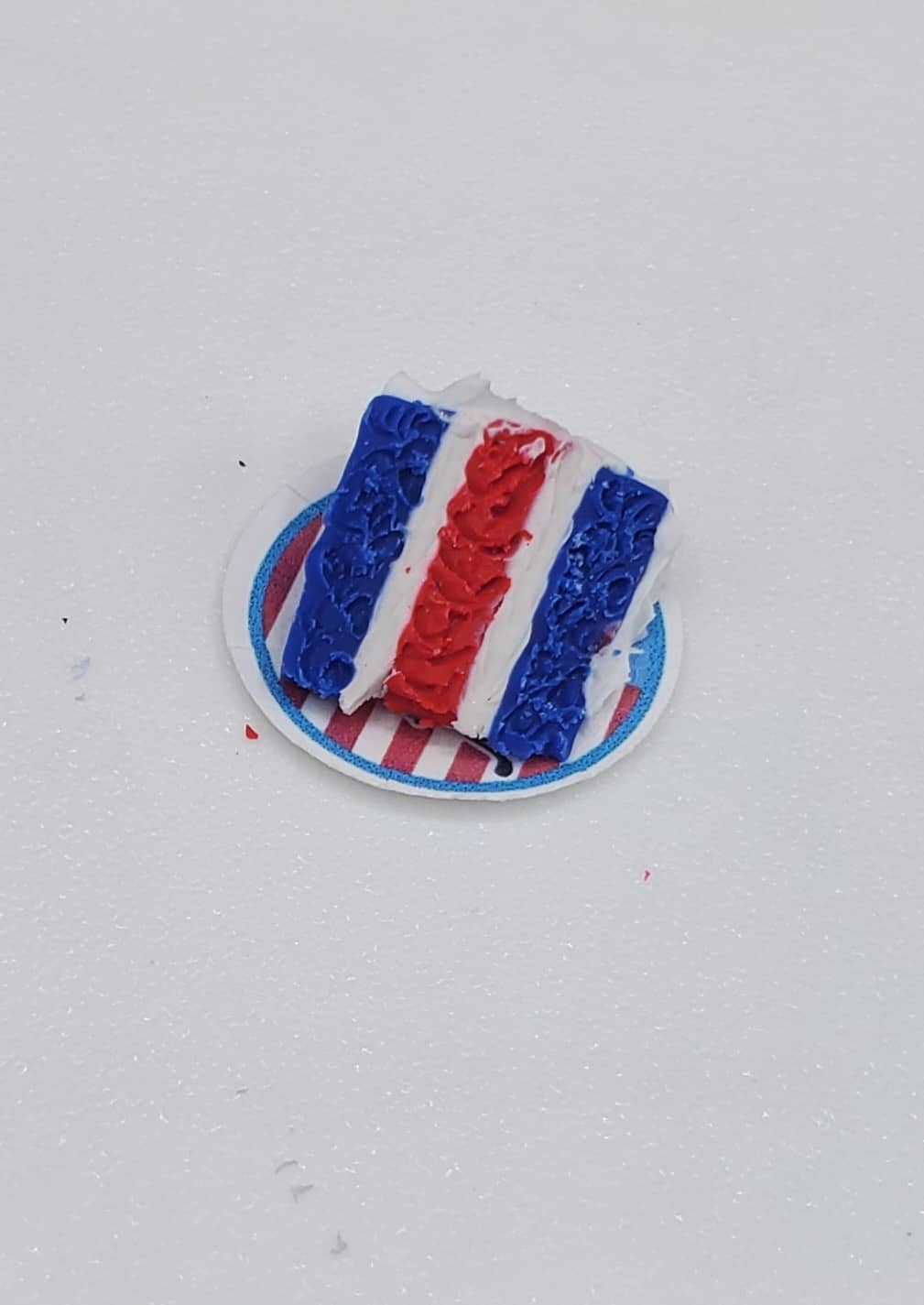 Small cake with red, white, and blue frosting on a white plate against a light gray background