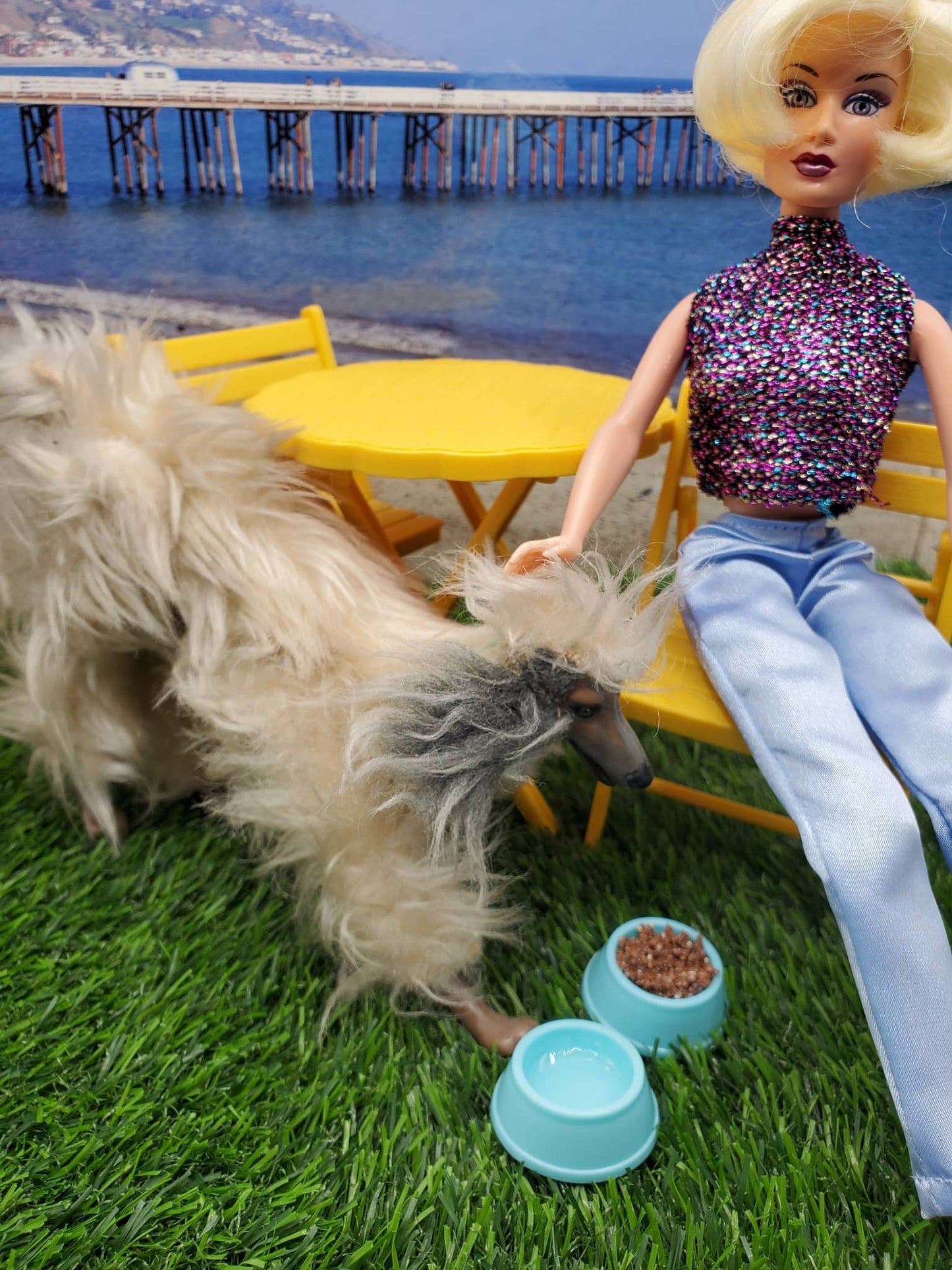 Fashion doll with Chef Gina's fashion doll dog food bowls beside a playful dog on a sunny patio