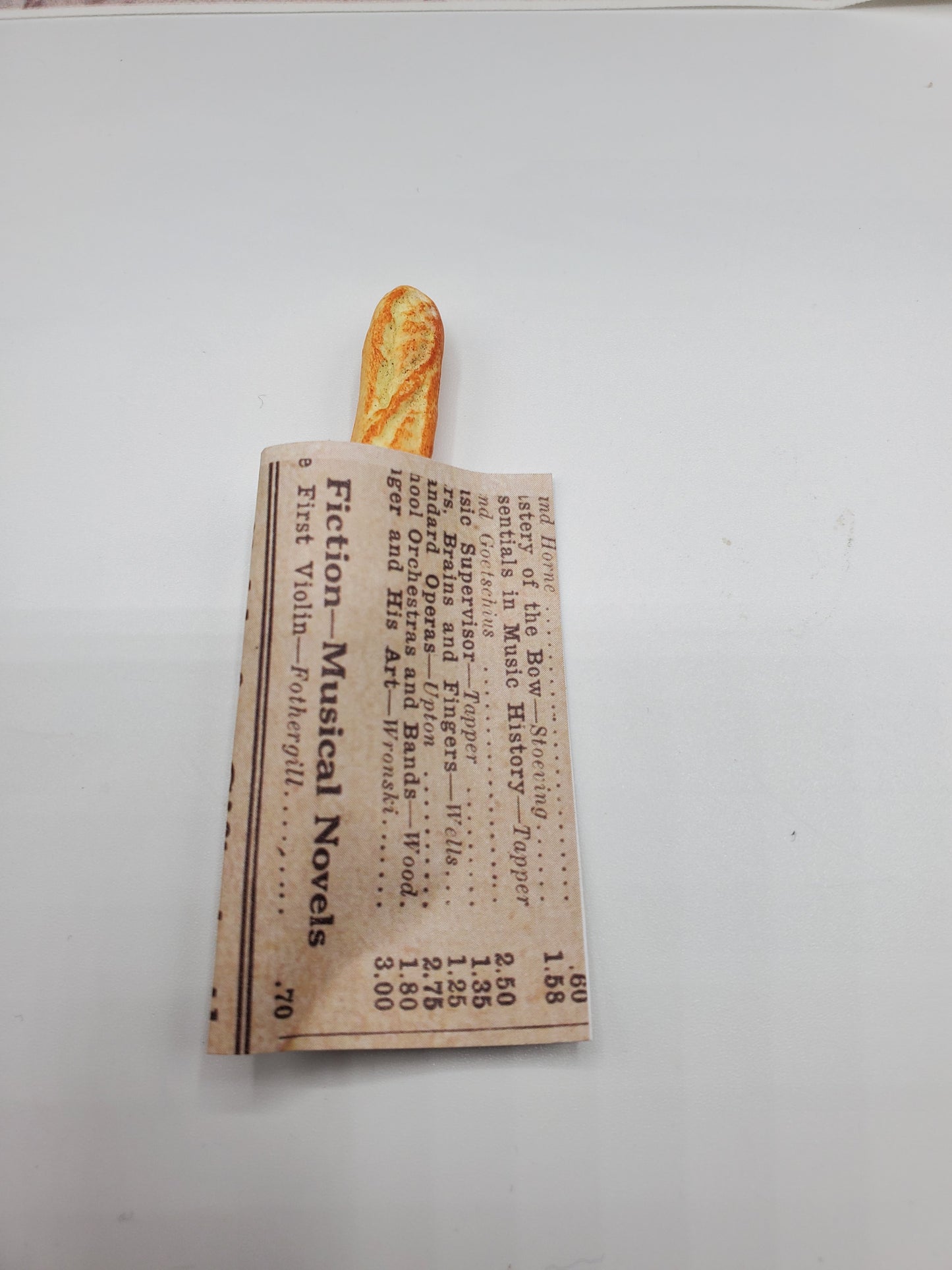 Chef Gina's miniature baguette bread wrapped in a newspaper-style paper on a white background