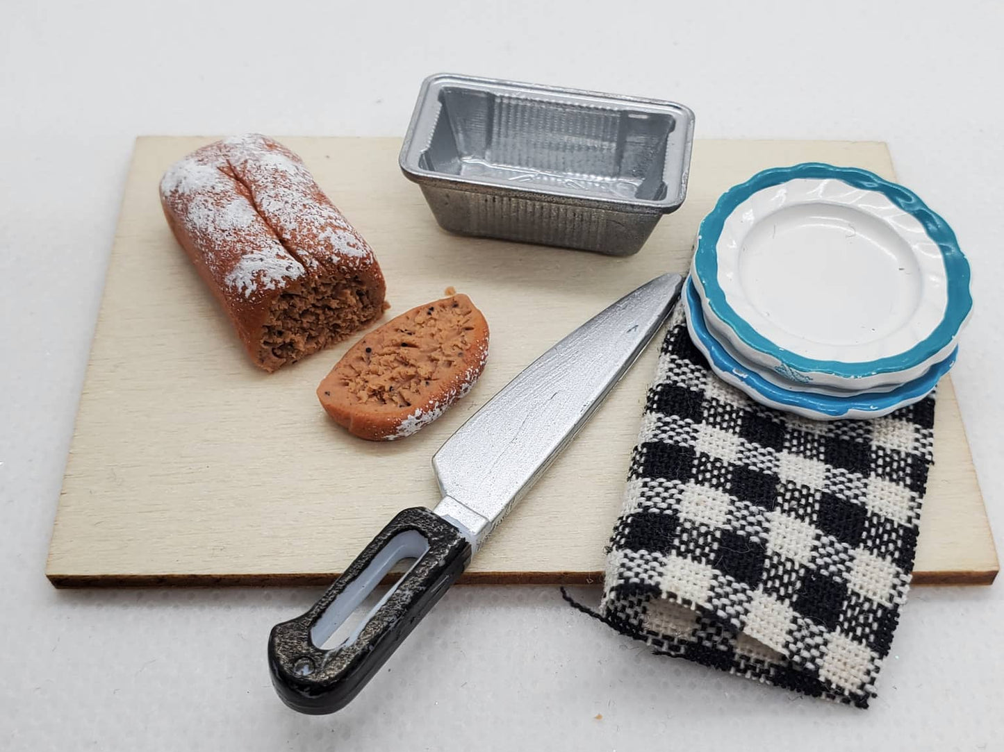 Miniature banana bread for dolls with slice, knife, and plates on a wooden cutting board