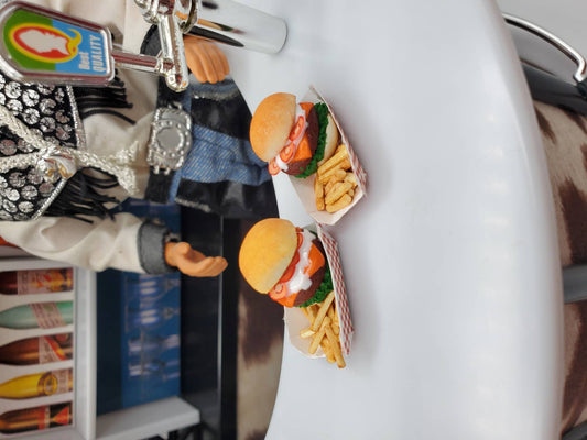 Two miniature bison burgers for dolls served with fries on a white counter next to a doll figure