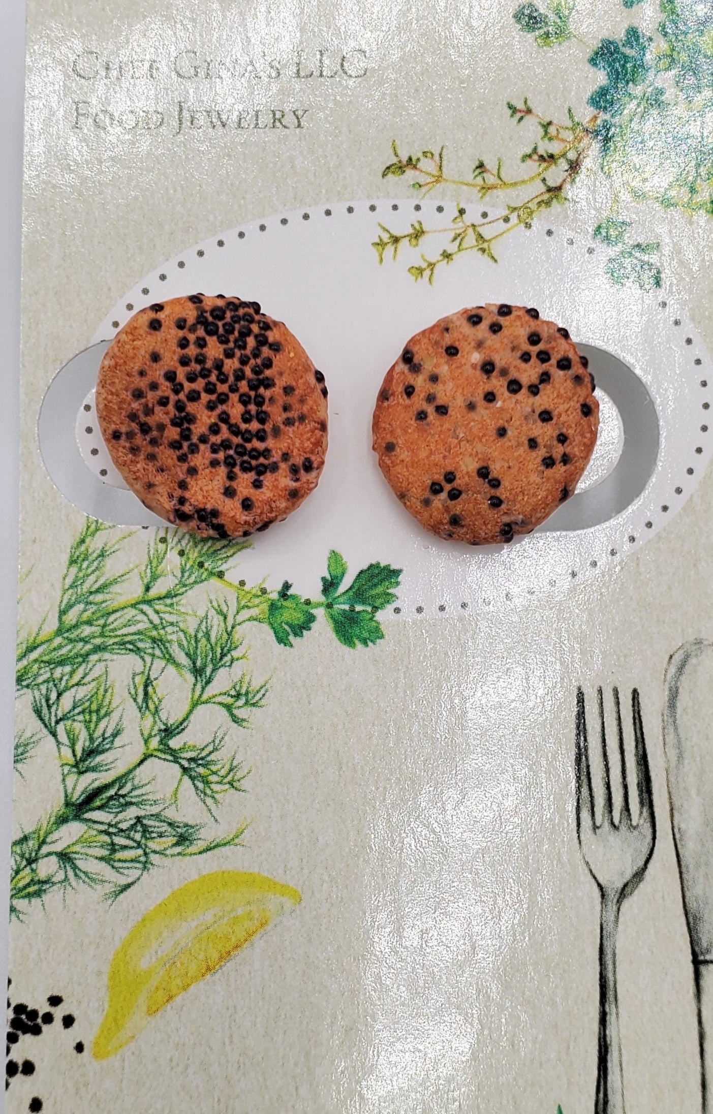 Chef Gina's miniature chocolate chip cookie earrings displayed on decorative card with herb and utensil design