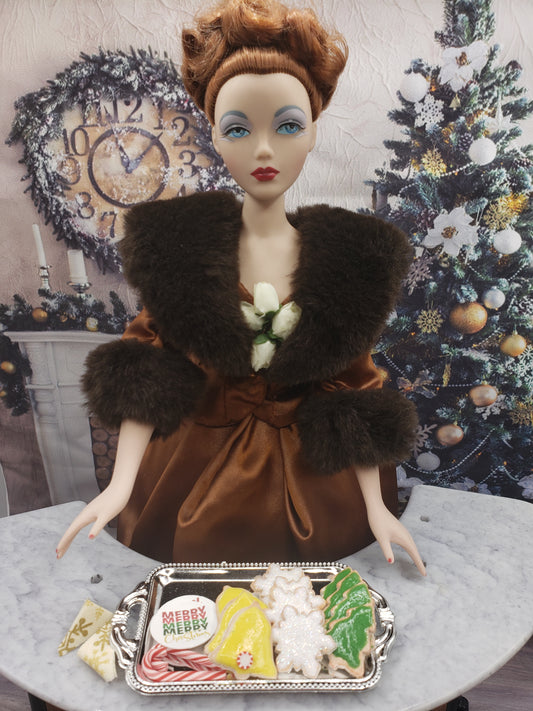 Miniature Christmas cookies for dolls on silver tray with doll dressed in brown vintage outfit and Christmas tree background