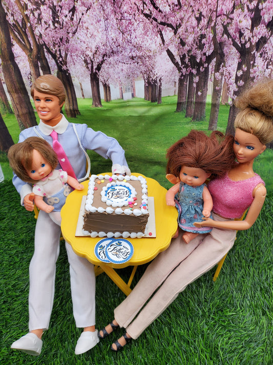 Miniature Father's Day cake on a table with dolls celebrating outdoors in a park setting