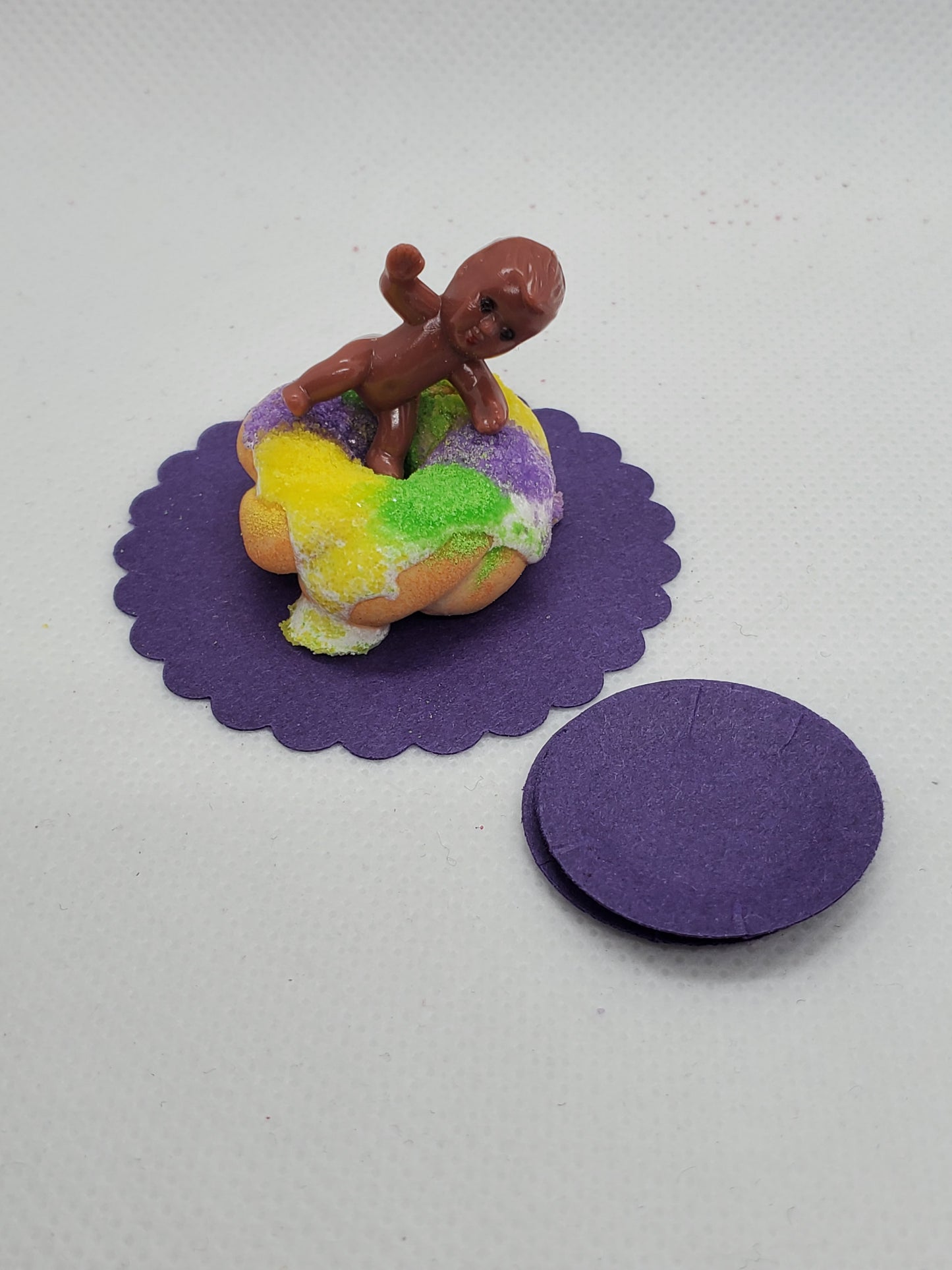 Miniature Mardi Gras king cake with vibrant icing and a toy figure on top