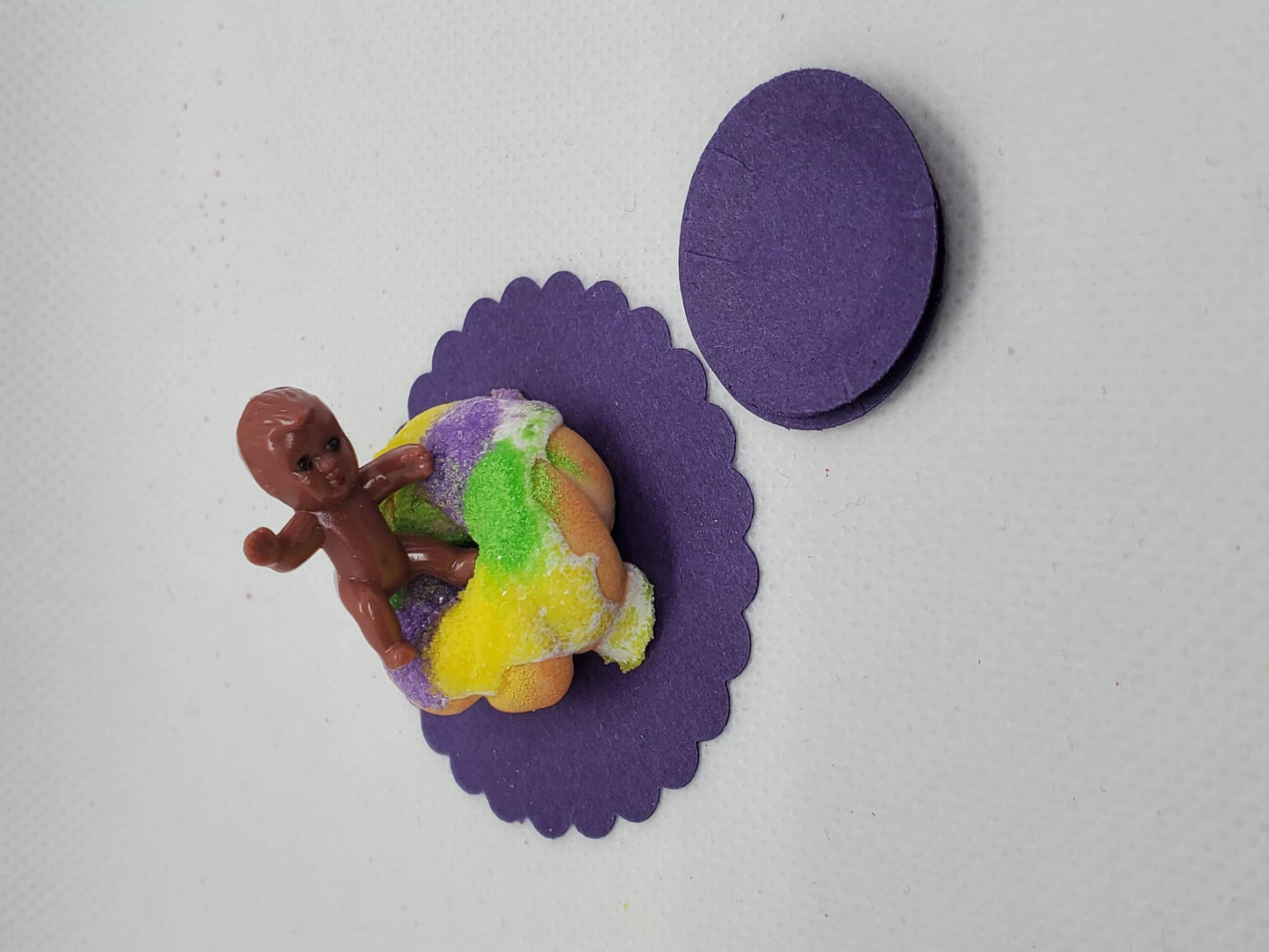 Miniature Mardi Gras king cake with vibrant icing and a toy figure on top