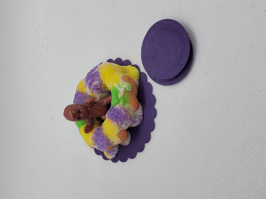 Miniature Mardi Gras king cake topped with a baby figurine and colorful sprinkles on a purple base