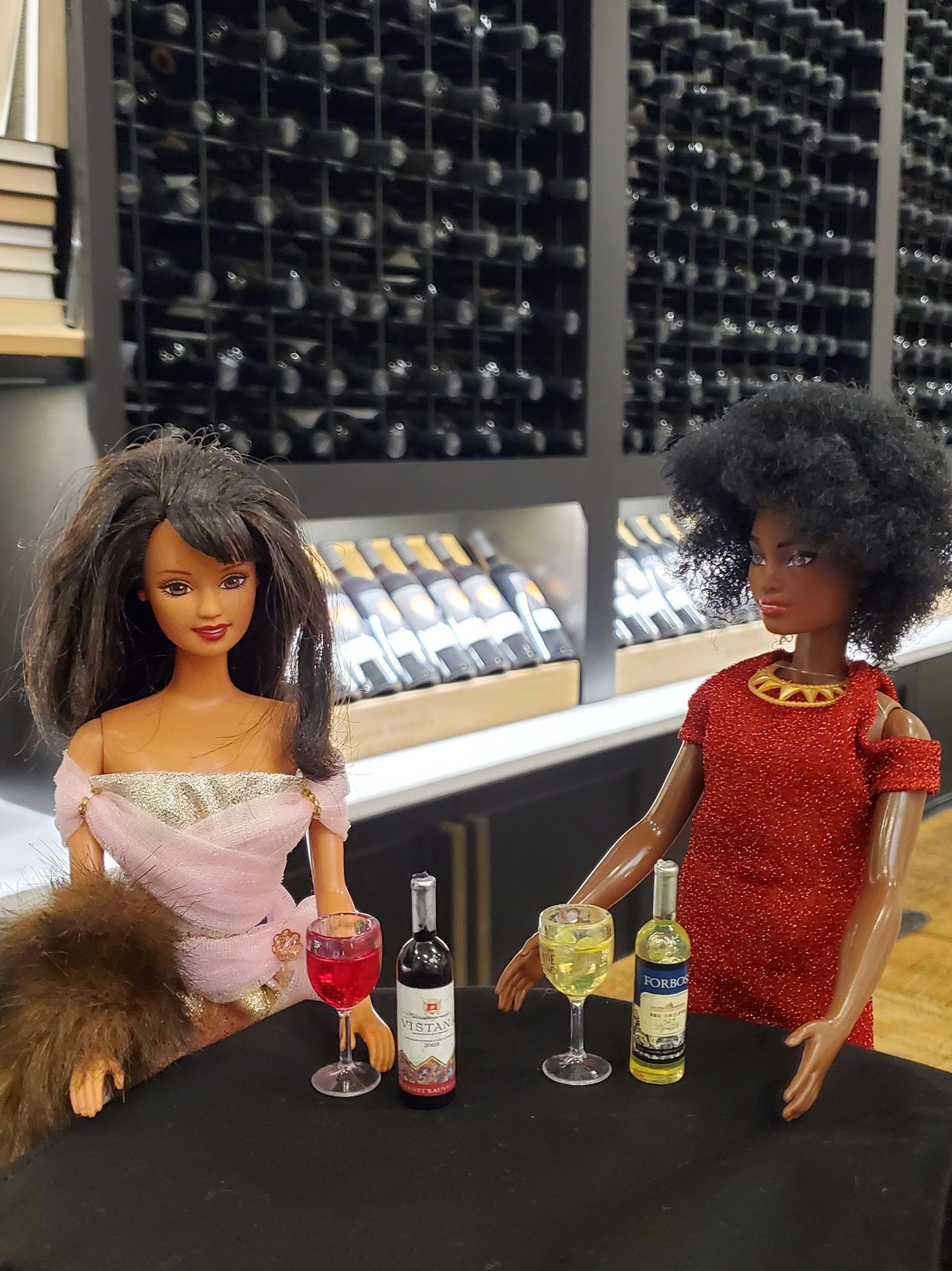 Two dolls at a table with miniature orange wine for dolls and wine glasses in a wine cellar setting