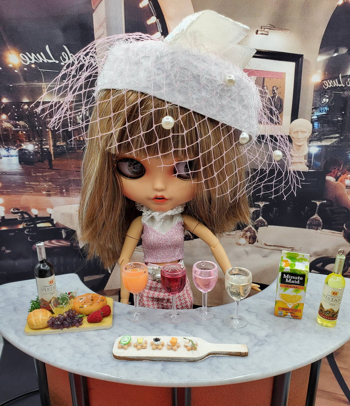 Miniature wine cheese tray hors d'oeuvres displayed with doll and drinks on marble table
