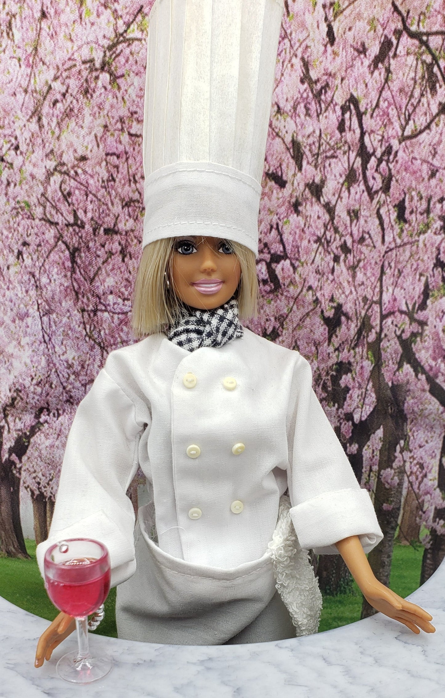 Chef doll in white uniform holding 1 6 scale wine glass for dolls with pink drink on marble table