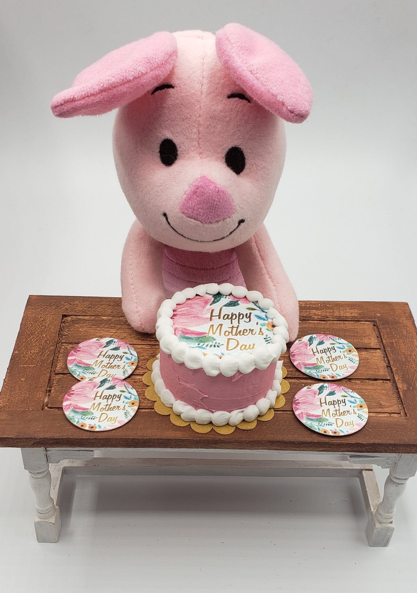 Chefginas miniature Mother's Day cake with pink frosting and a stuffed pig holding it on a table