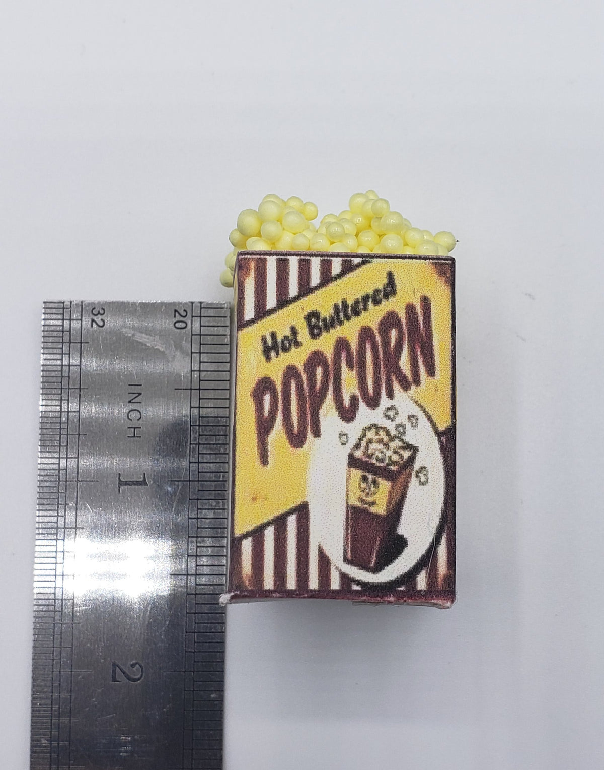 Chef Gina's miniature popcorn tub with hot buttered popcorn design next to ruler for size scale