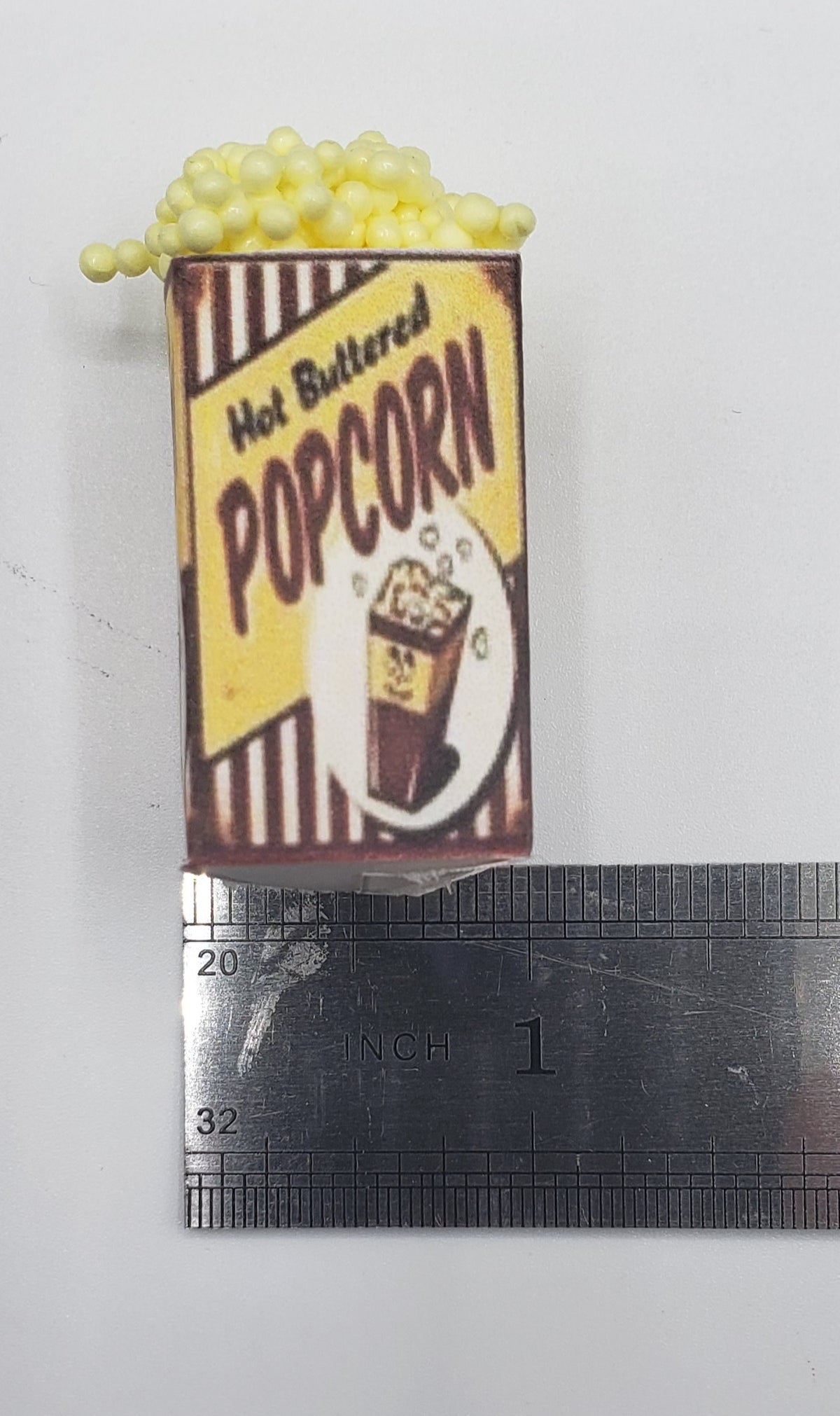 Chef Gina's miniature popcorn tub with hot buttered popcorn design next to a ruler for size reference