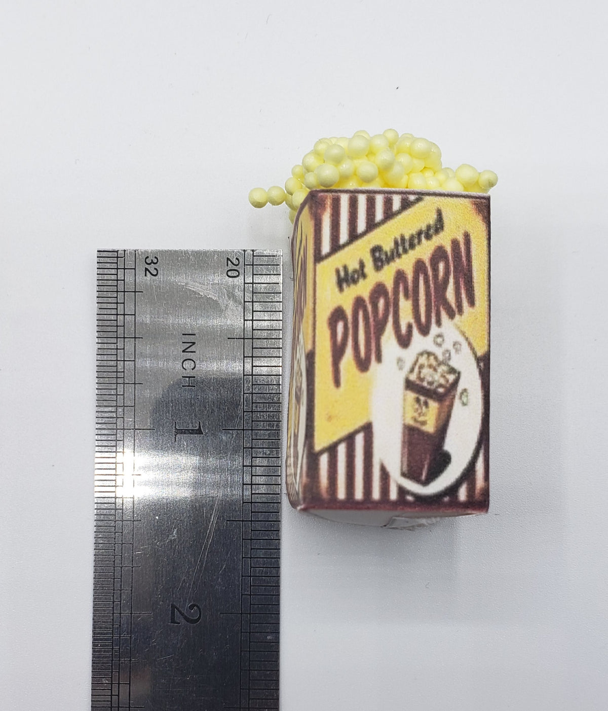 miniature popcorn tub with hot buttered popcorn design next to a ruler for size reference