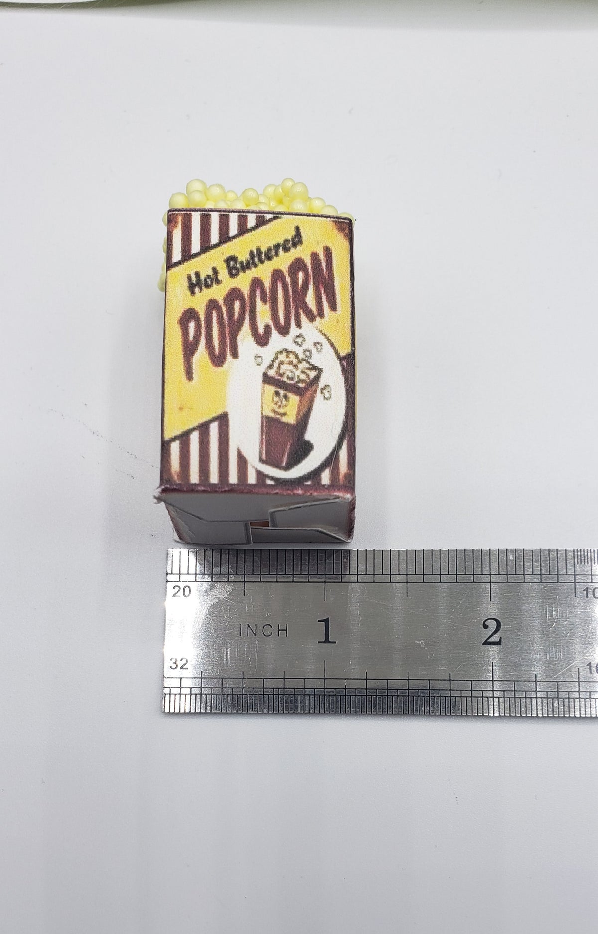 Chef Gina's miniature popcorn tub carnival food prop with hot buttered popcorn design next to ruler