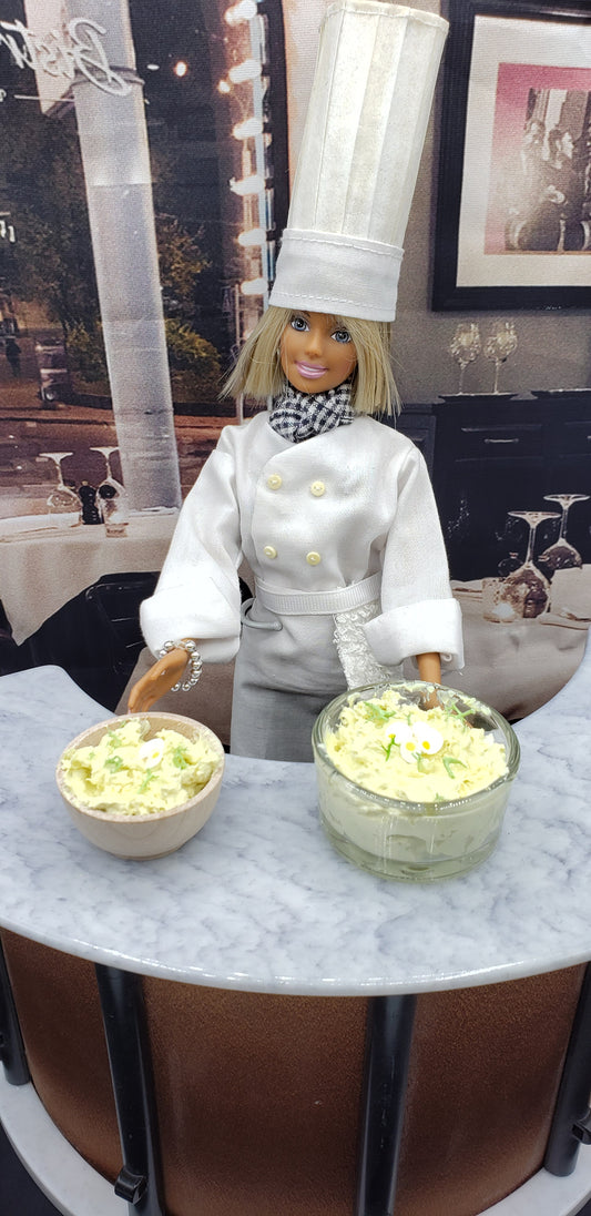 Chef doll presenting a miniature potato salad bowl alongside a larger serving bowl in a restaurant setting