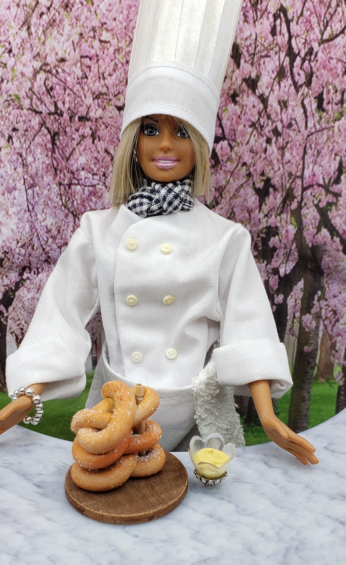 Chef Gina's Mini Food Doll with a miniature pretzel tower on a wooden platter in a scenic background