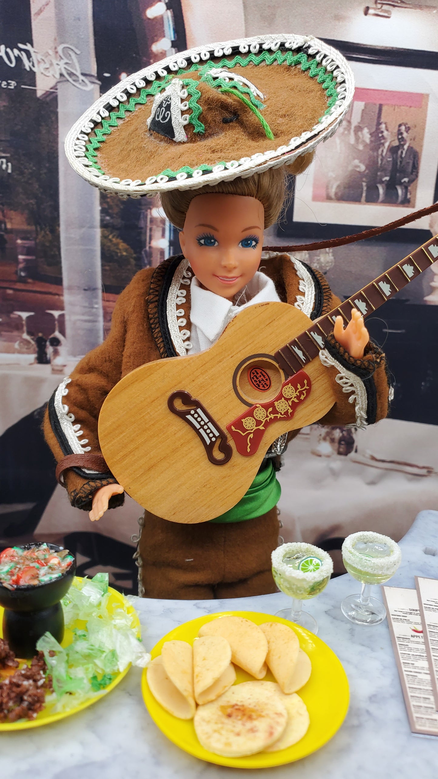 Doll with guitar and sombrero in front of a table with food
