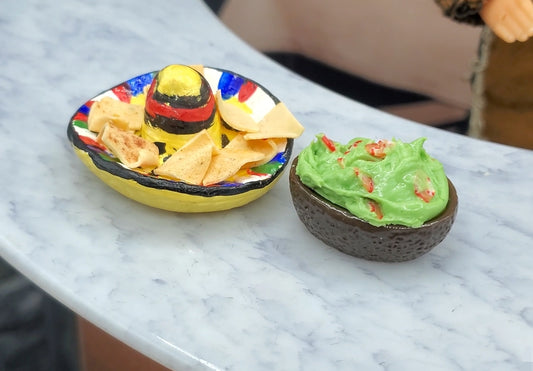 Two small bowls with decorative designs, one containing chips and the other guacamole, on a marble surface.