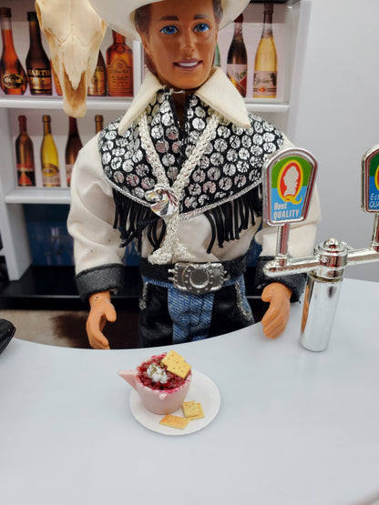 Cup of Chili with Crackers For Dolls served in a miniature pink bowl on a white plate next to a cowboy doll at a bar