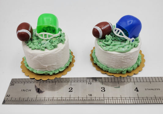 Miniature football cake by Chef Gina's with green and blue helmets on white frosting desserts next to a ruler