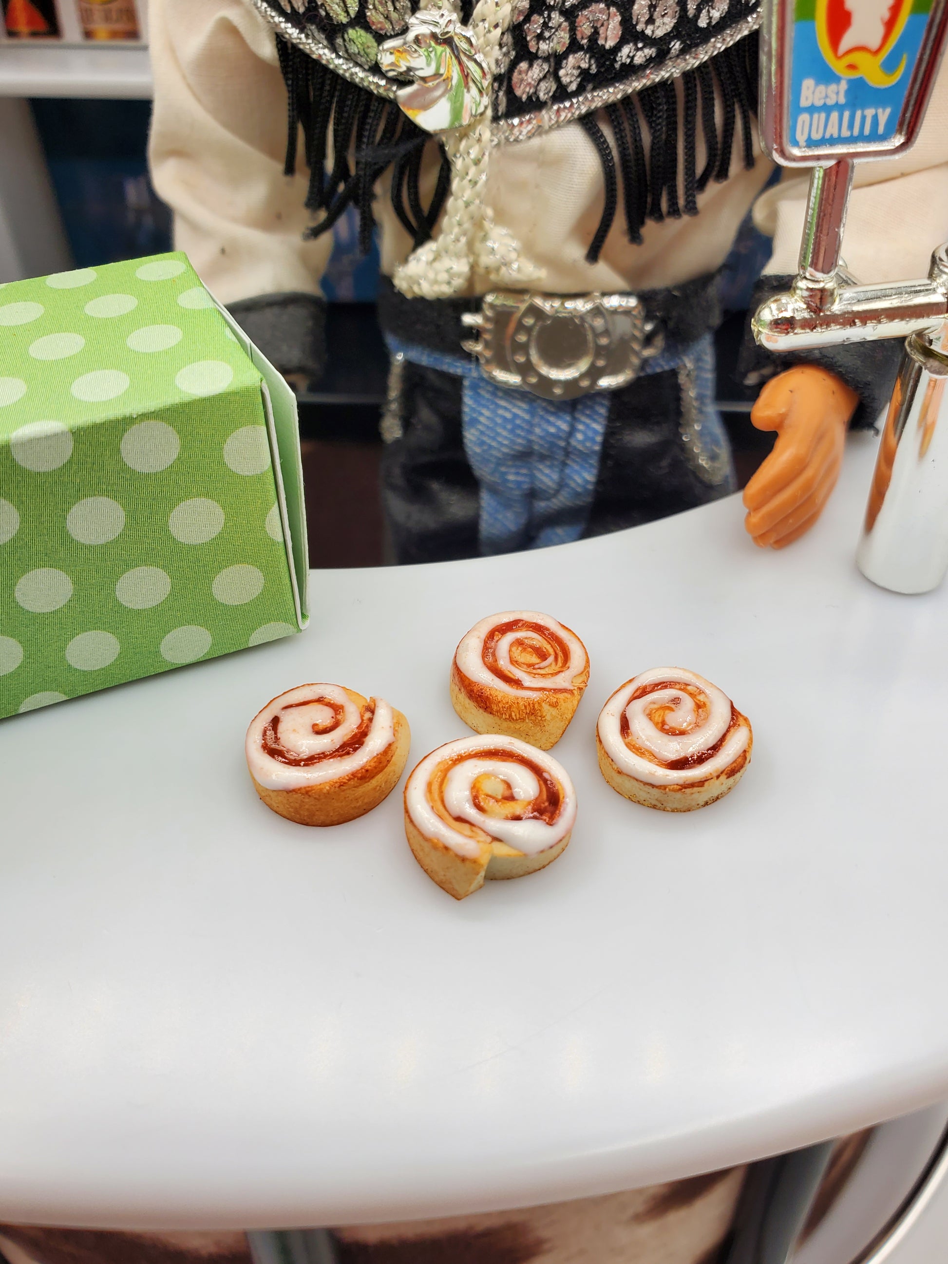 Miniature Texas cinnamon rolls for Fashion dolls displayed on a white surface with a green polka dot box nearby