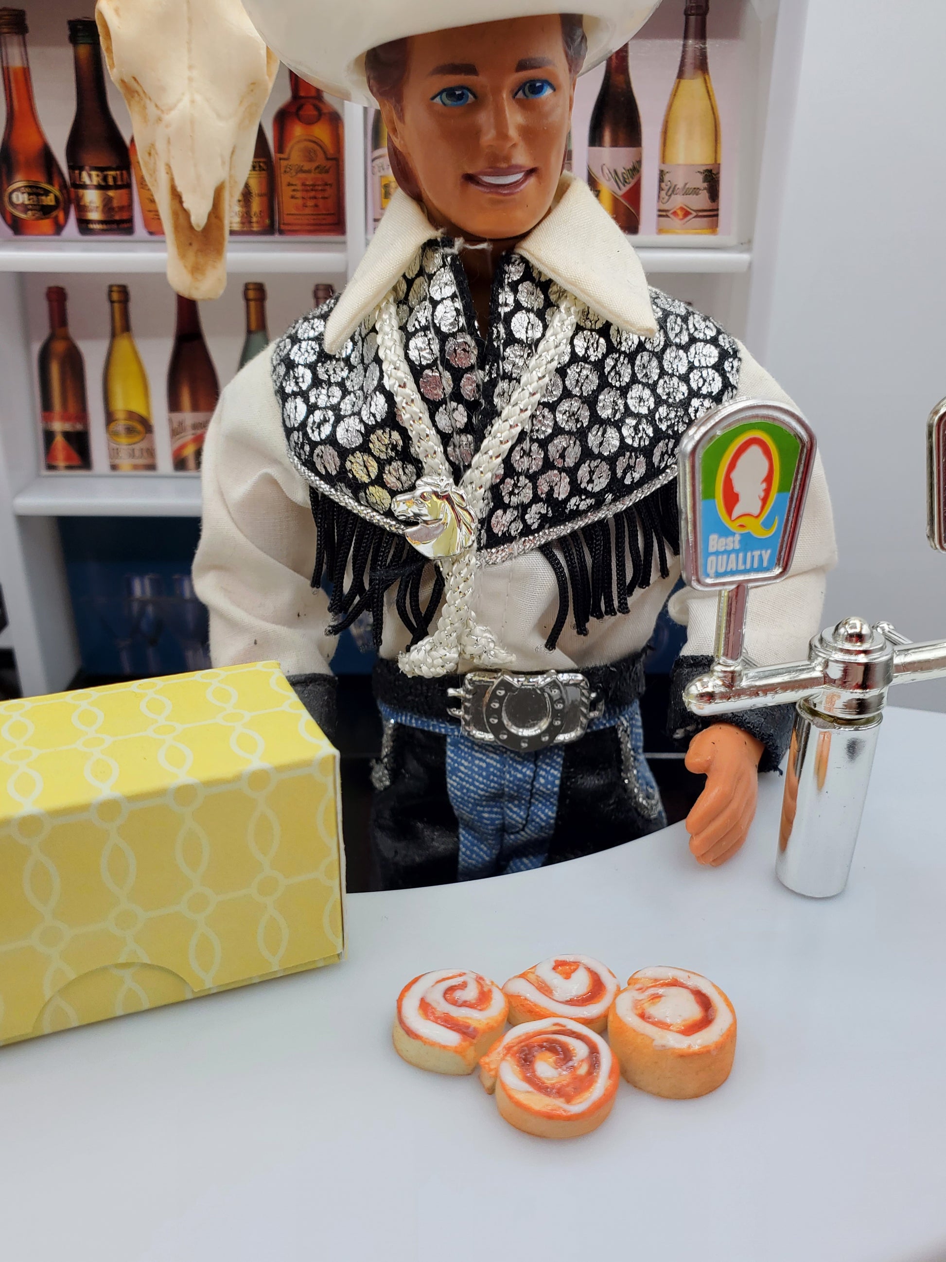 Miniature Texas cinnamon rolls for Fashion dolls displayed with a cowboy doll in western attire and a yellow box