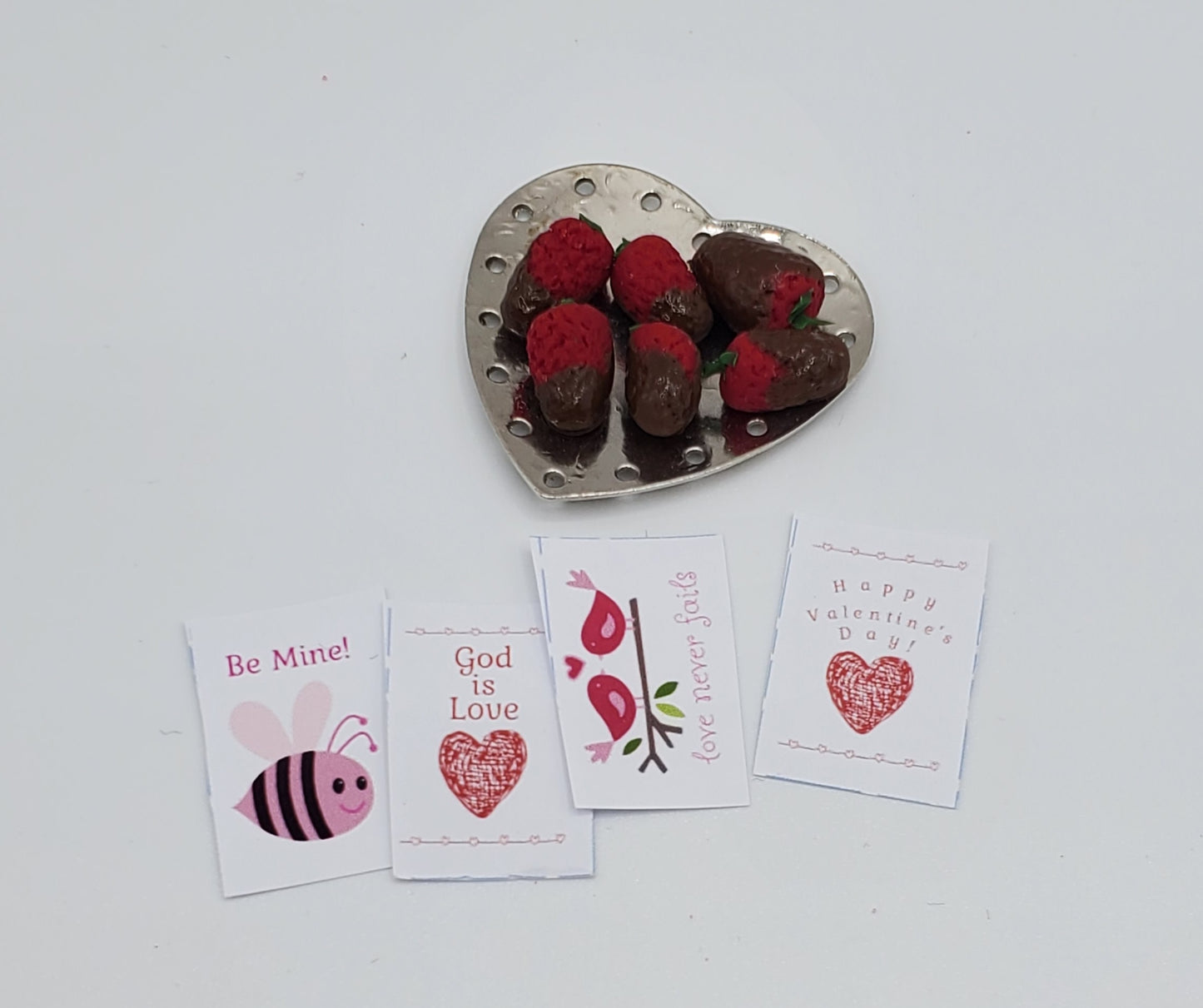 Heart-shaped dish with chocolate-dipped strawberries and Valentine's Day cards on a white background