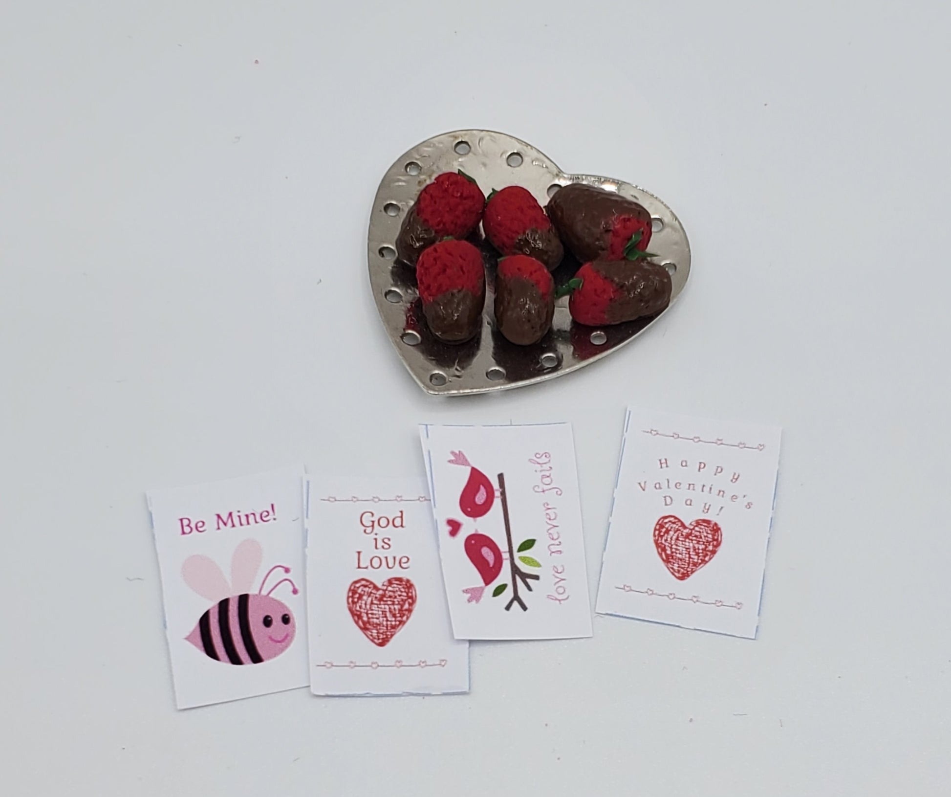 Heart-shaped dish with chocolate-dipped strawberries and Valentine's Day cards on a white background