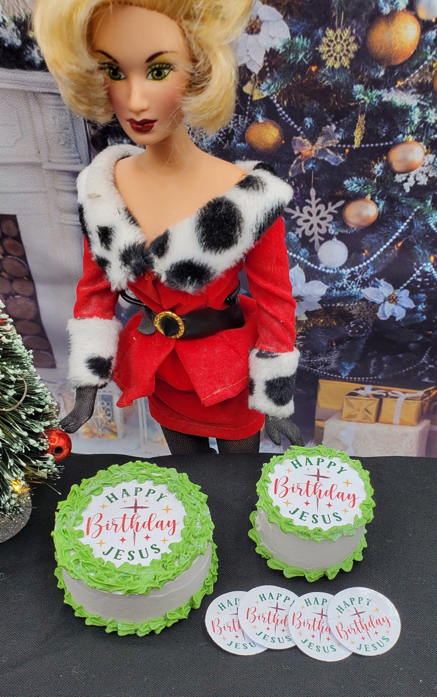Barbie doll in a red outfit with fur trim standing next to two birthday cakes and 'Happy Birthday Jesus' signs.