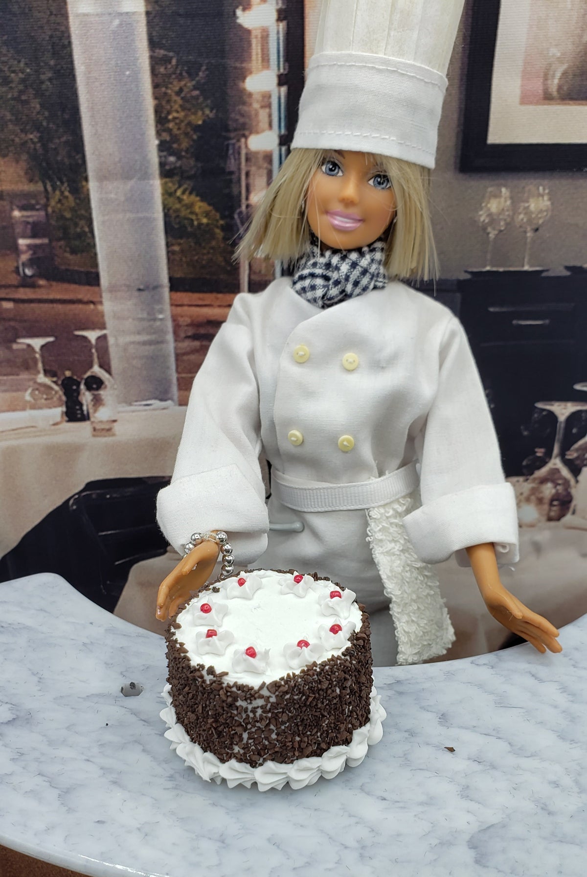 Chef doll with miniature blackforest cake decorated with whipped cream and cherries on a marble countertop