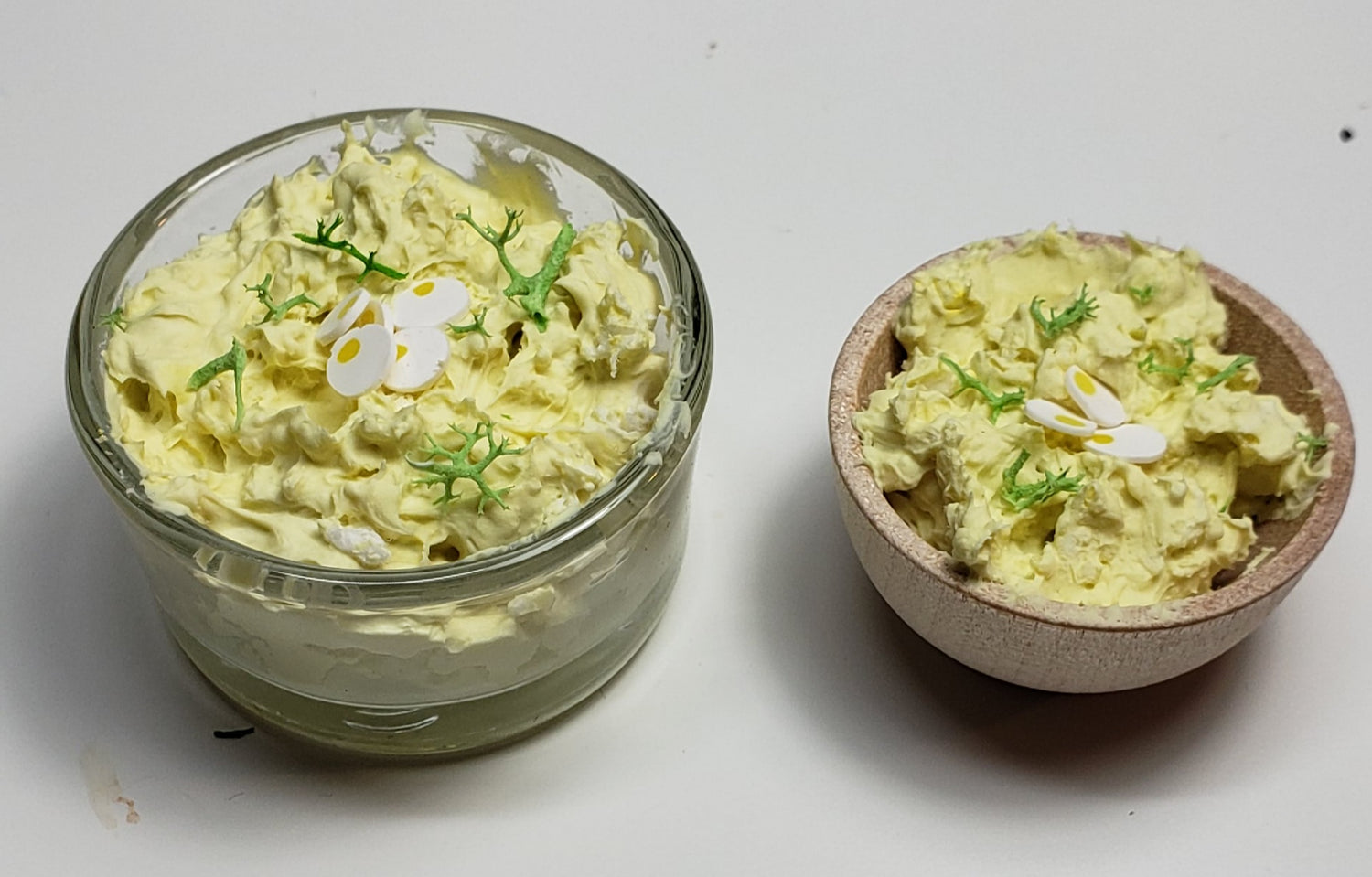 Two serving bowls of miniature potato salad bowl, one glass and one wooden, garnished with herbs and flowers